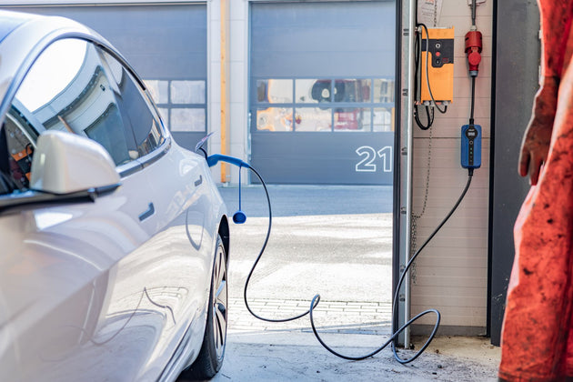 White Tesla charging in front of a garage with a blue Voldt EV charging cable